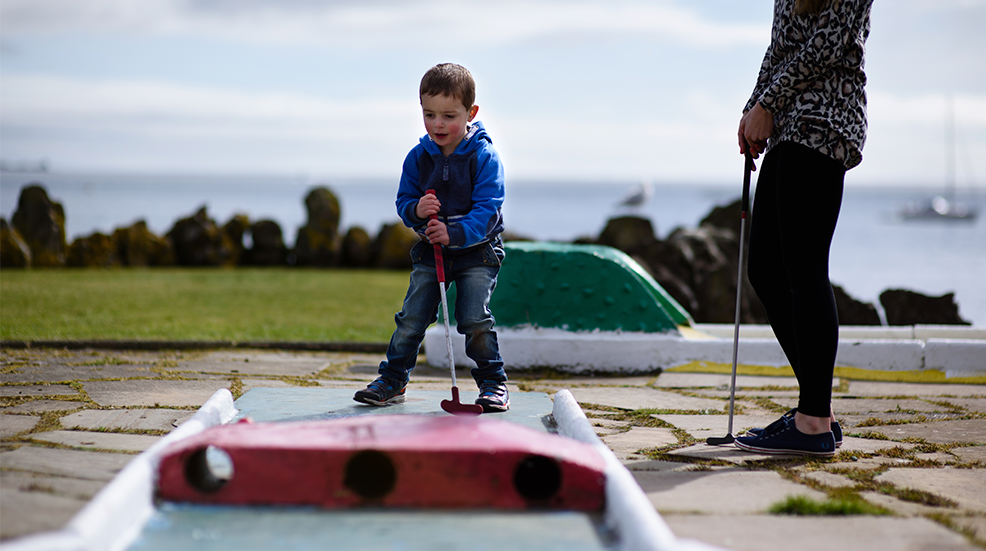 Image of a three and a half year old playing crazy golf outside.